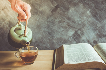 Teapot pouring tea into the cup with reading book