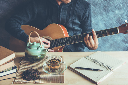 Young man composing the song with guitar on table with tea cupの写真素材