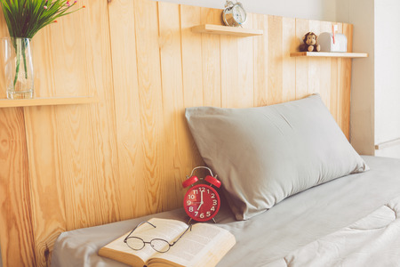 Alarm clock on bed with book and glasses at morning timeの写真素材