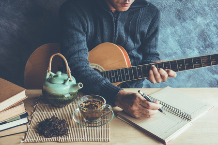 Young man composing the song with guitar on table with tea cupの写真素材