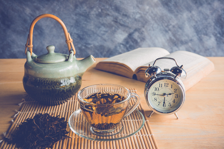A cup of tea and tea pot  with clock and book in tea time on tableの写真素材