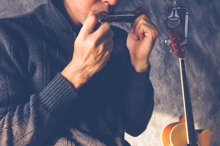 A man playing mouthorgan with guitar background