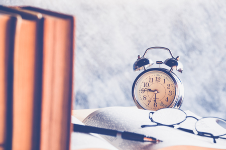 Retro clock with old books and vintage glasses on a wooden tableの写真素材