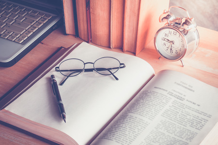 A pencil and glasses put on open old book on wood table with sunlightの写真素材