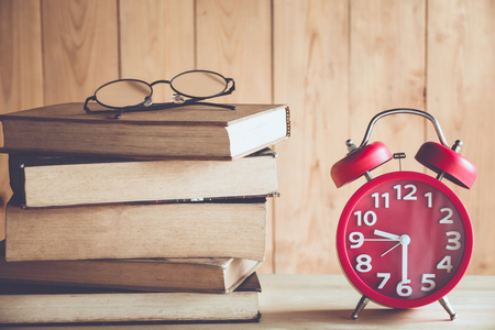 Education concept. Alarm clock with old books and eyeglasses , wood backgroundの写真素材