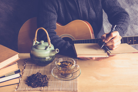 Young man composing the song with guitar on table with tea cupの写真素材