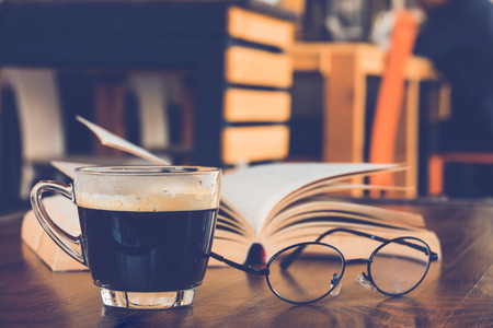 A cup of black coffee with book and glasses on table in coffee shopの写真素材
