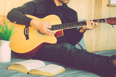 Young man playing the guitar after reading a book.の写真素材