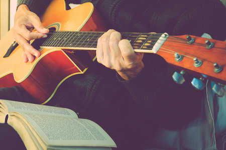 Young man playing the guitar after reading a book.