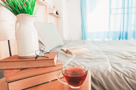 Book and a cup of tea on bed in bedroom