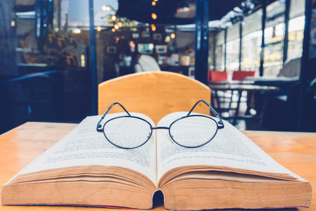 Reading glasses on table with open book in cafeの写真素材