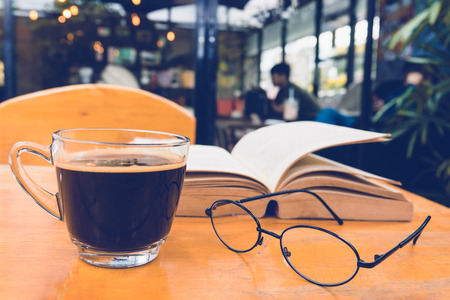 A cup of black coffee with reading glasses on table and open book in cafeの写真素材