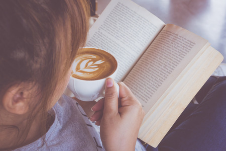Young woman reading a book and drinking a cup of coffee