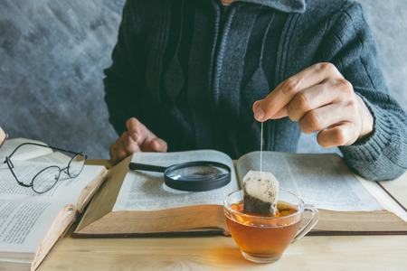 A man  brewing tea bag with glass of tea on table in reading timeの写真素材