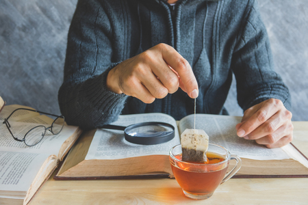 A man  brewing tea bag with glass of tea on table in reading timeの写真素材