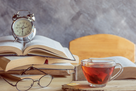 A cup of tea with glasses and  alarm clock on stack booksの写真素材