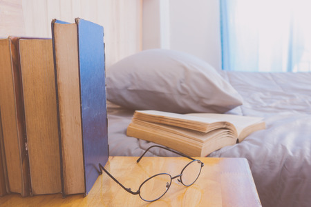 Open book on bed with row books and eye glasses foregroundの写真素材