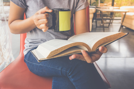 Young woman reading a book and holding cup of coffeeの写真素材