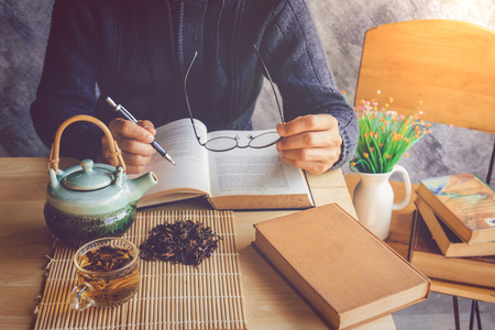 A man reading book  with cup of tea and old book on tableの写真素材