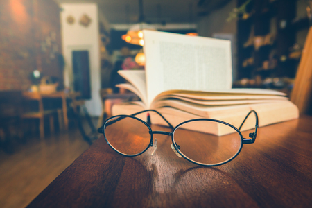 Reading glasses on table with open book in cafeの写真素材