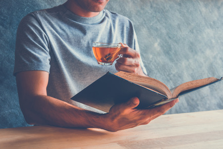 A man reading a book with a cup of tea on tableの写真素材