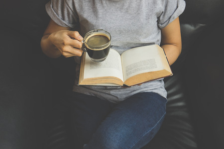Young woman reading a book and holding cup of coffeeの写真素材