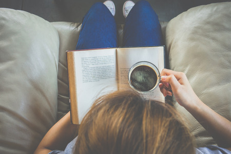 Top view of young woman reading a book and holding cup of coffeeの写真素材