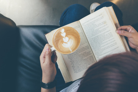Top view of young woman reading a book and holding cup of coffeeの写真素材