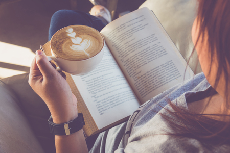 Young woman reading a book and holding cup of coffeeの写真素材