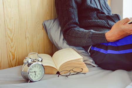 Relaxing time at morning with young man reading book in bed at houseの写真素材