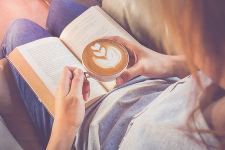 Soft photo of young girl reading a book and drinking coffee, top viewの写真素材
