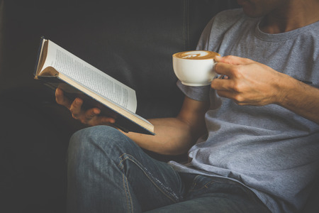 A man reading a book and holding cup of coffeeの写真素材