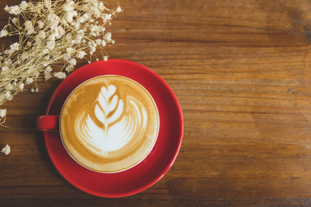 A red cup of coffee with vintage flower on wood table in coffee shopの写真素材
