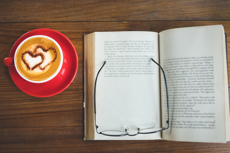 A cup of coffee cappuccino or latte with open book and glasses on topの写真素材