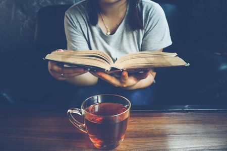 A glass of tea on table with woman reading book on sofa