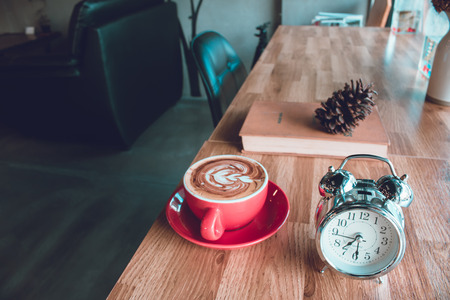 A cup of coffee latte with alarm clock and textbook on table in cafeの写真素材