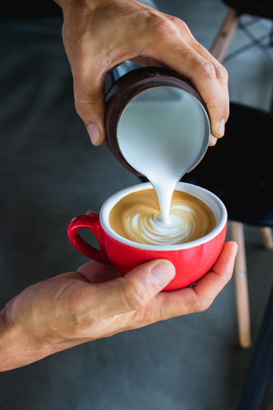 Pouring milk from pitcher make coffee latte art by Barista in coffee shopの写真素材
