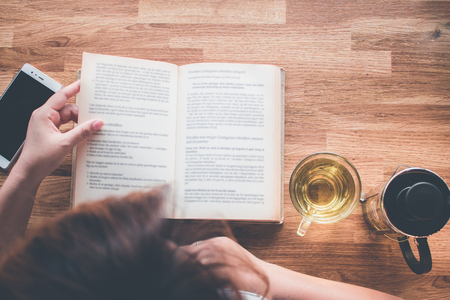 A girl reading a book with cup of tea and tea pot