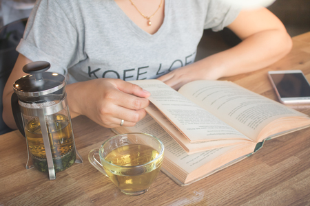 A girl reading a book and holding a cup of tea wit tea pot on table in cafeの写真素材