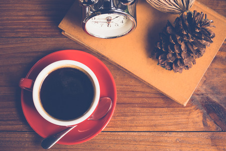 Black coffee in red cup with book and clock on table in cafeの写真素材