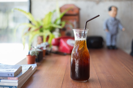 Cold black coffee with ice in bottle on wood table in coffee shopの写真素材