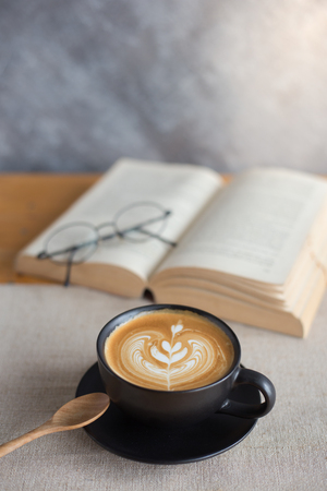 A cup of latte coffee with book on wood tableの写真素材