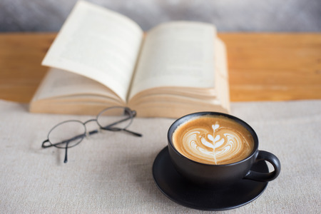 A cup of latte coffee with book on wood tableの写真素材
