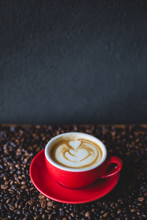 A red cup of coffee with latte  on coffee bean with stone backgroundの写真素材