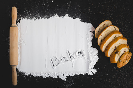 Rolling pin with flat flour and bread on black chalkboard with word "bake" from above.の写真素材
