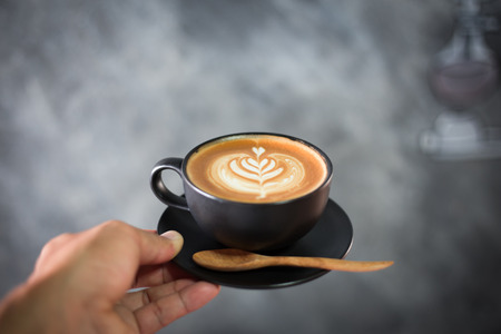 Hand holding cappuccino or latte coffee with blurred loft backgroundの写真素材