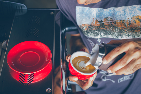 Pouring cream milk into a cup of coffee making latte artの写真素材