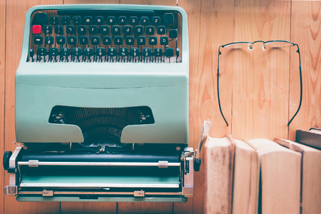 Retro typewriter and old vintage books with reading glasses on wooden tableの写真素材