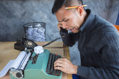 A man talking telephone with someone for mistake of work with typewriter he must new type again ,  bin backgruond has many mistake paperの写真素材