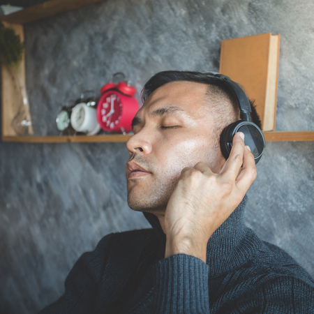 profile view of the head of a young male person listening to music on headphones while adjusting them with his handsの写真素材